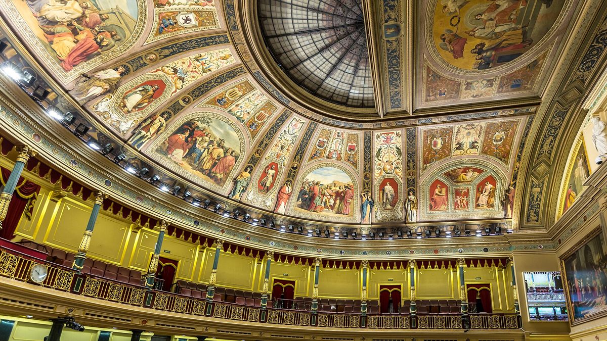 Interior del hemiciclo del Congreso de los Diputados: bóveda con frescos, lámparas y filas de escaños vacíos