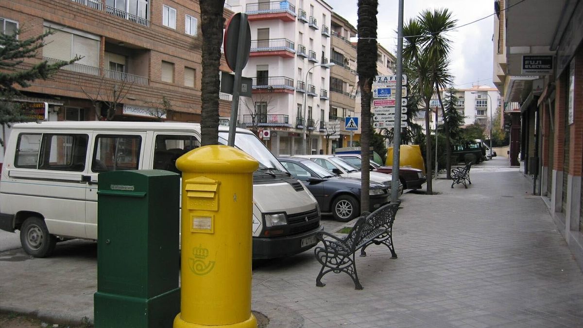 Buzón amarillo de Correos en la acera de una calle, con el logotipo de la empresa postal y el cartel del horario de recogida